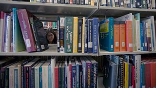 Image of two students through stacks of library books.